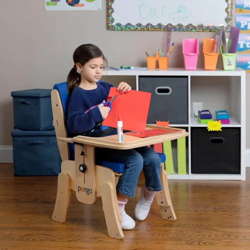 Child using scissors to cut red paper at a colorful craft table in a playroom